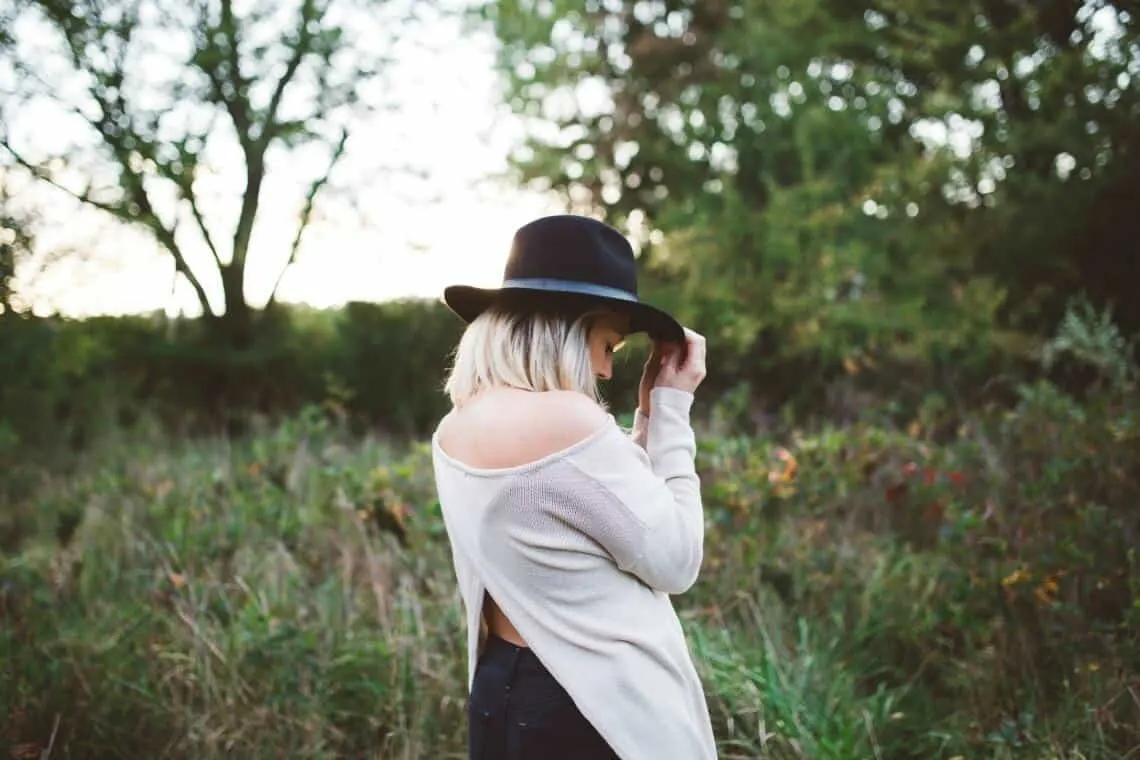 Woman holds brim of black hat outdoors.