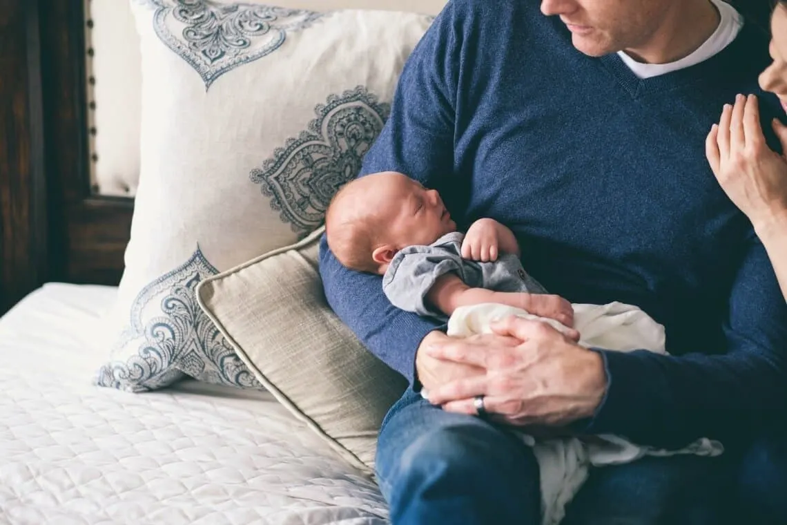 Couple holds newborn baby on couch.
