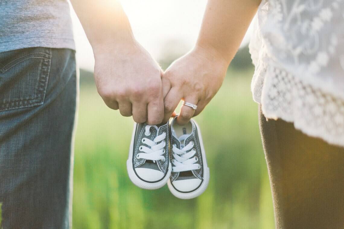 Couple holds blue baby shoes for pregnancy announcement.