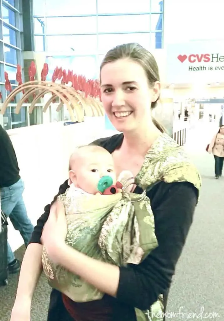 Mother holds baby in baby sling at airport.