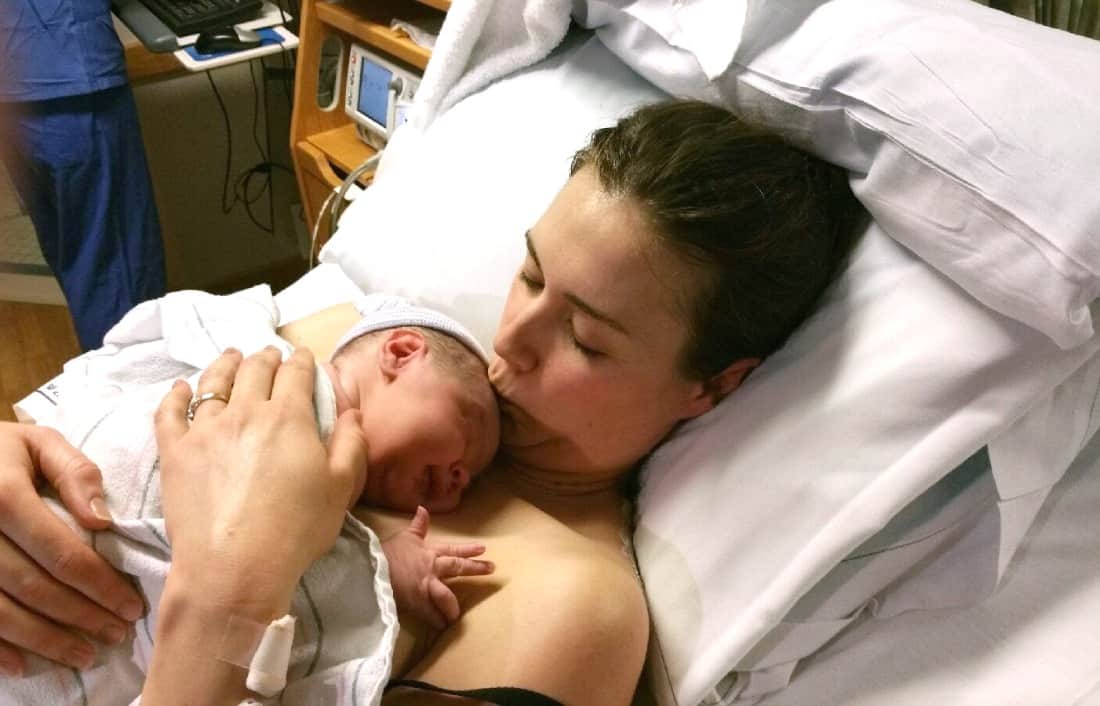 Mother holds newborn on hospital bed.