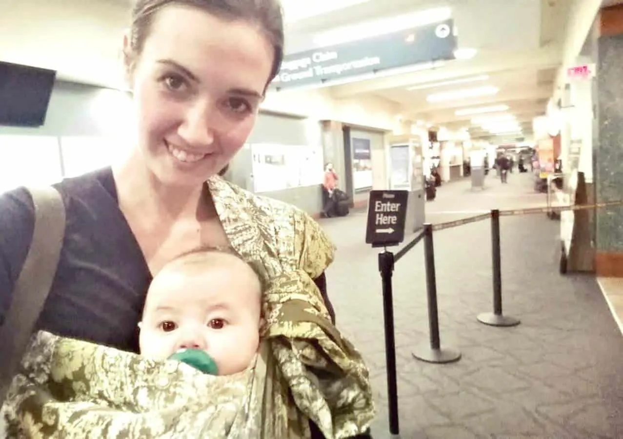 Mother holds baby using sling in airport.