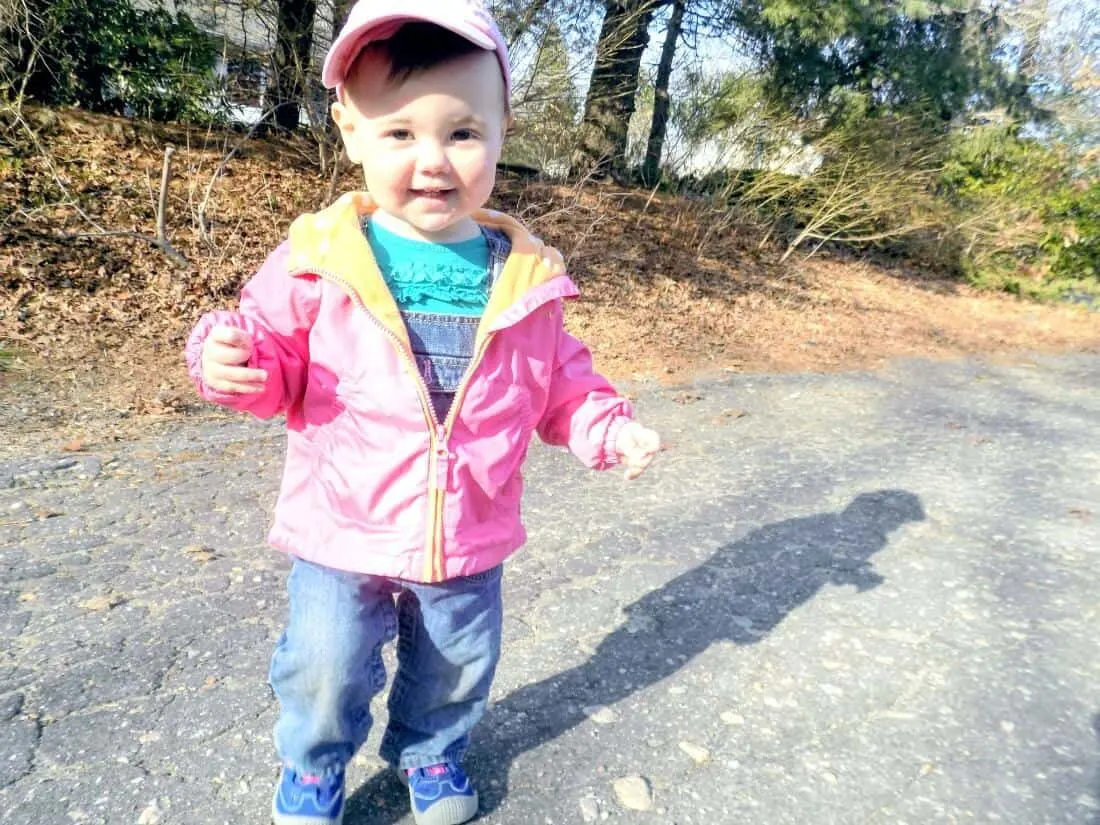Little girl plays outside in pink jacket.