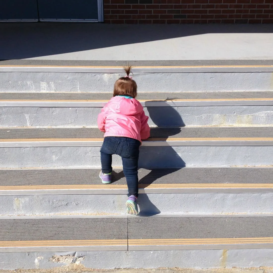 Toddler girl climb stairs outside.