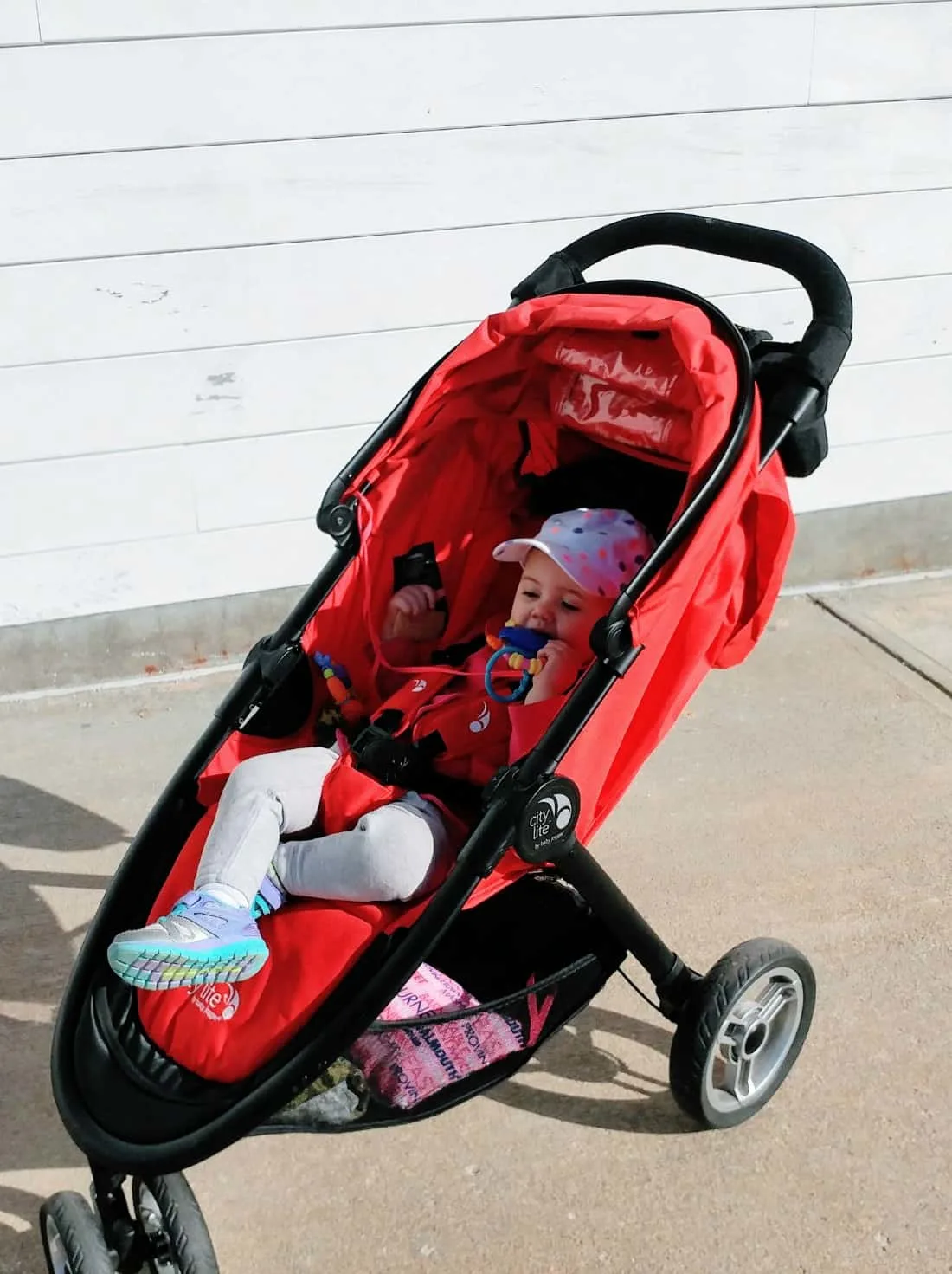 Baby girl plays in red stroller.