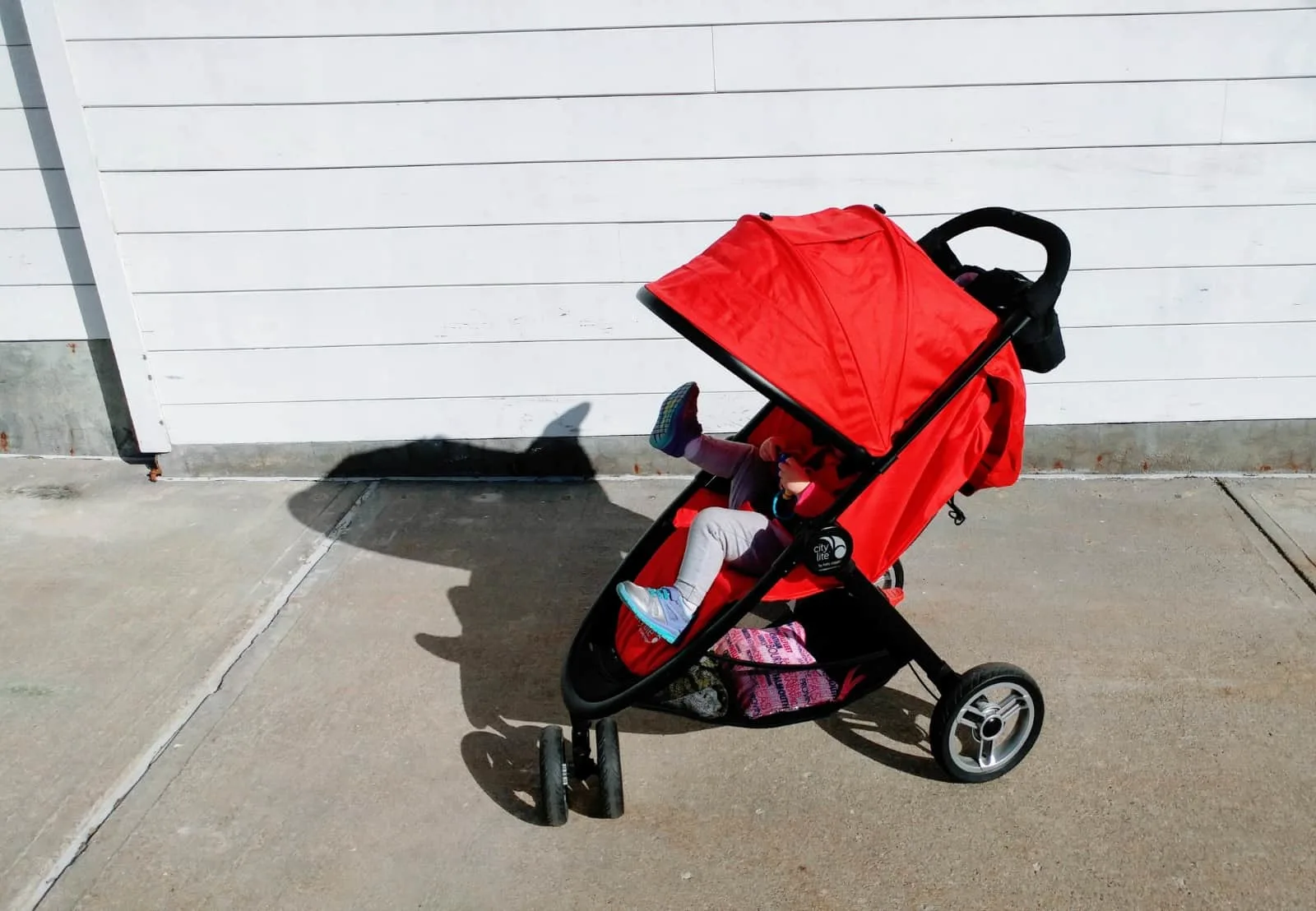 Toddler girl kicks legs up from red stroller.