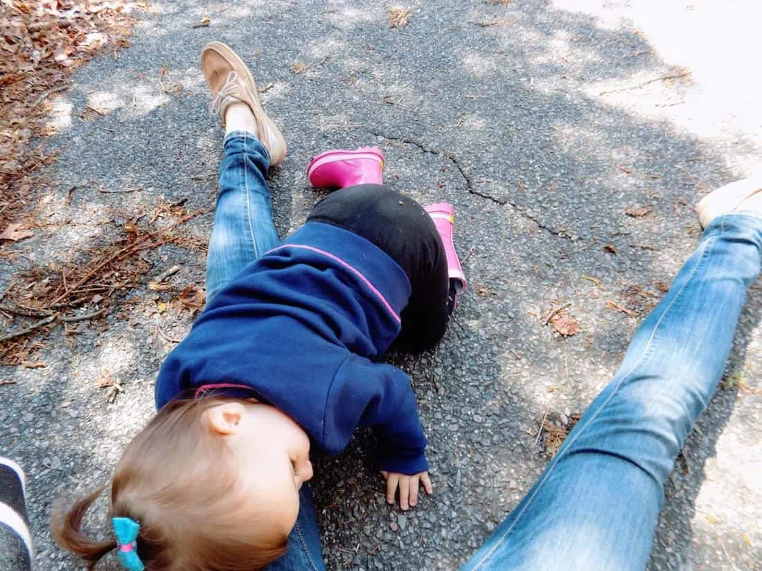 Little girl plays over moms legs on ground.