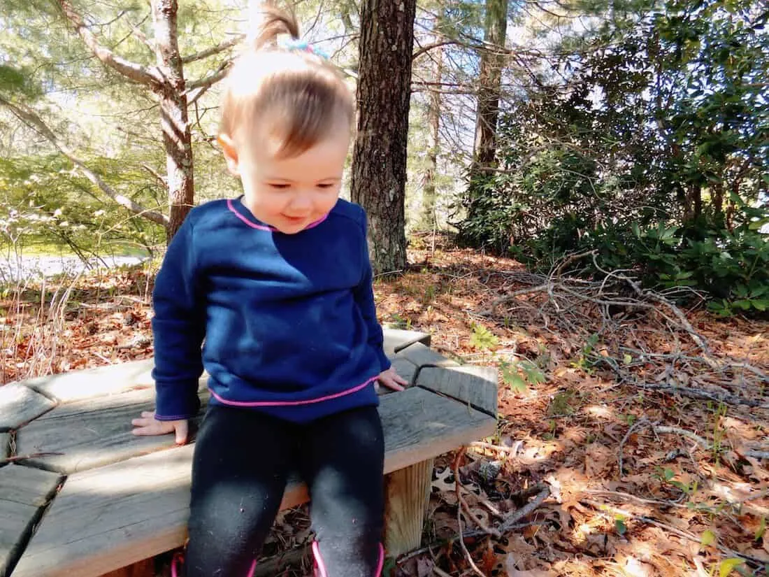 Little girl stands up from outdoor bench.