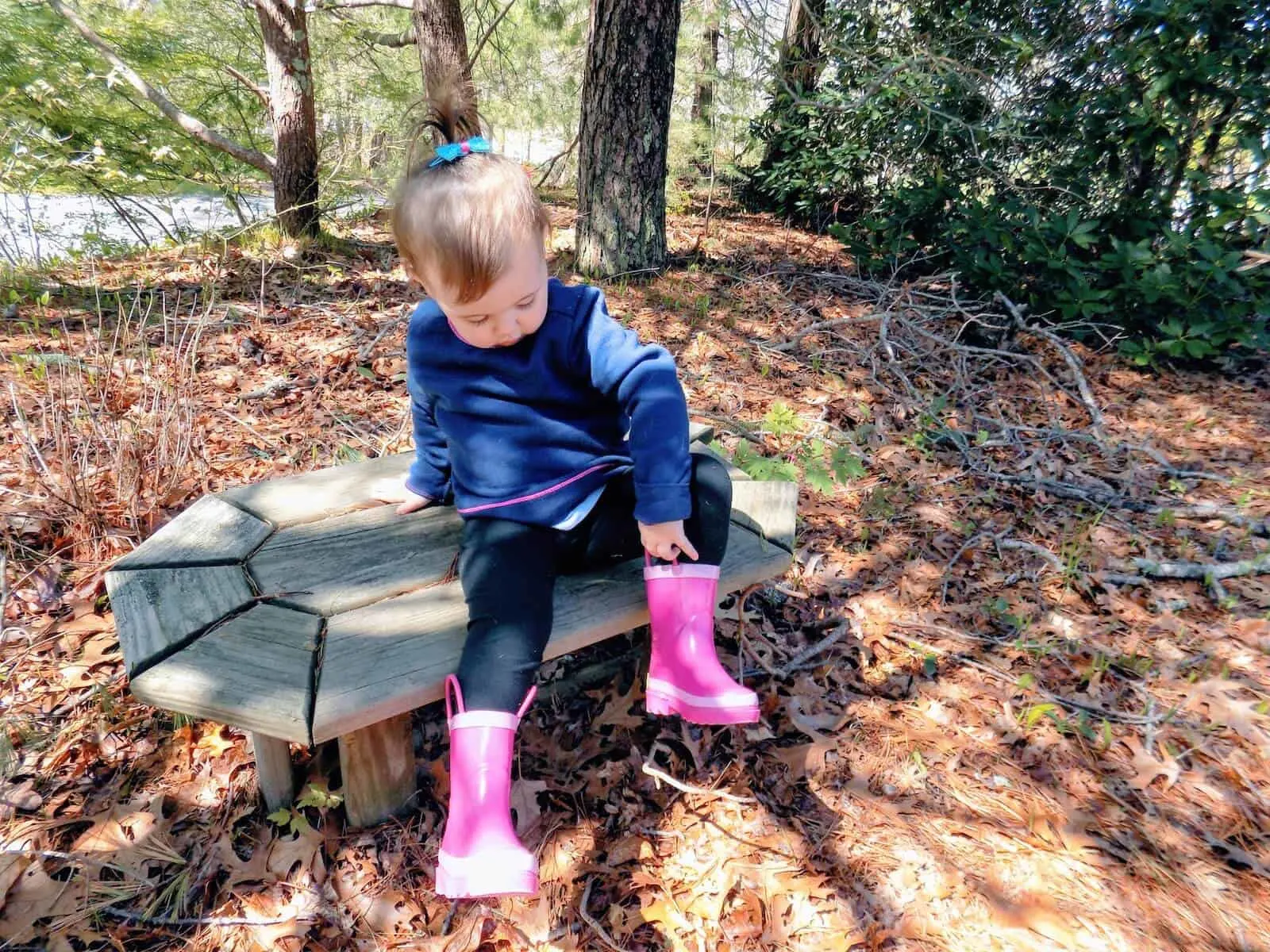 Toddler girl in pink boots sits on outdoor bench.