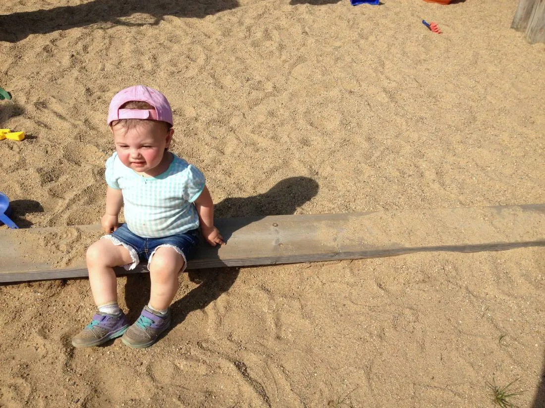 Toddler girl sits on log over sand.