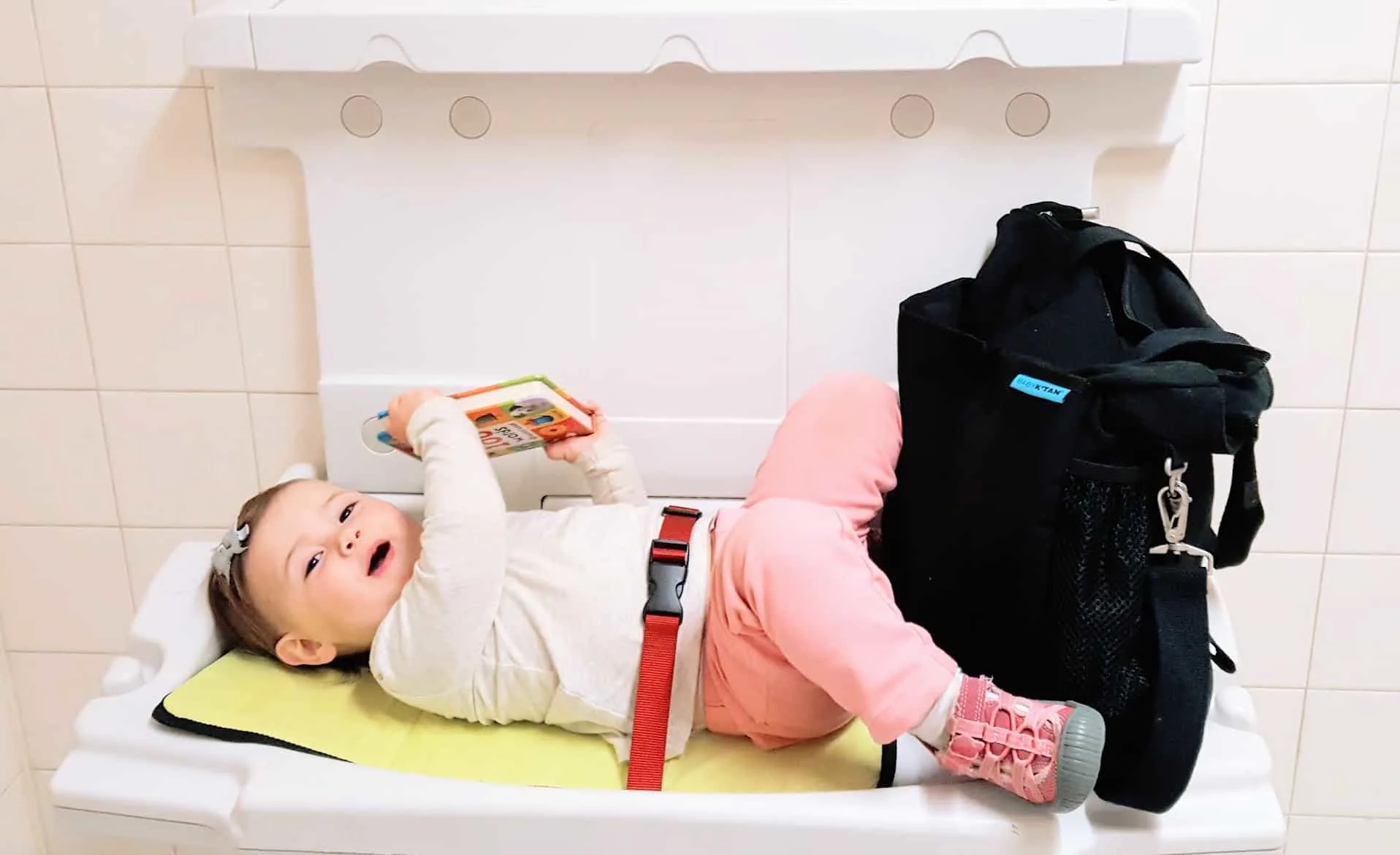 Baby on changing table next to diaper bag.