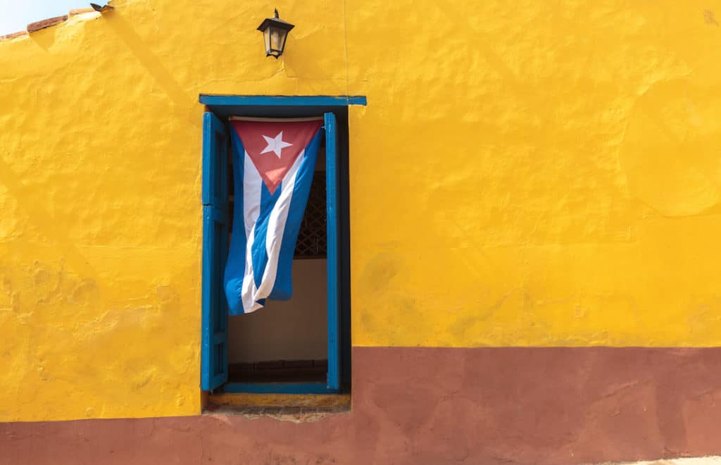Cuban flag waves from window of colorful building.