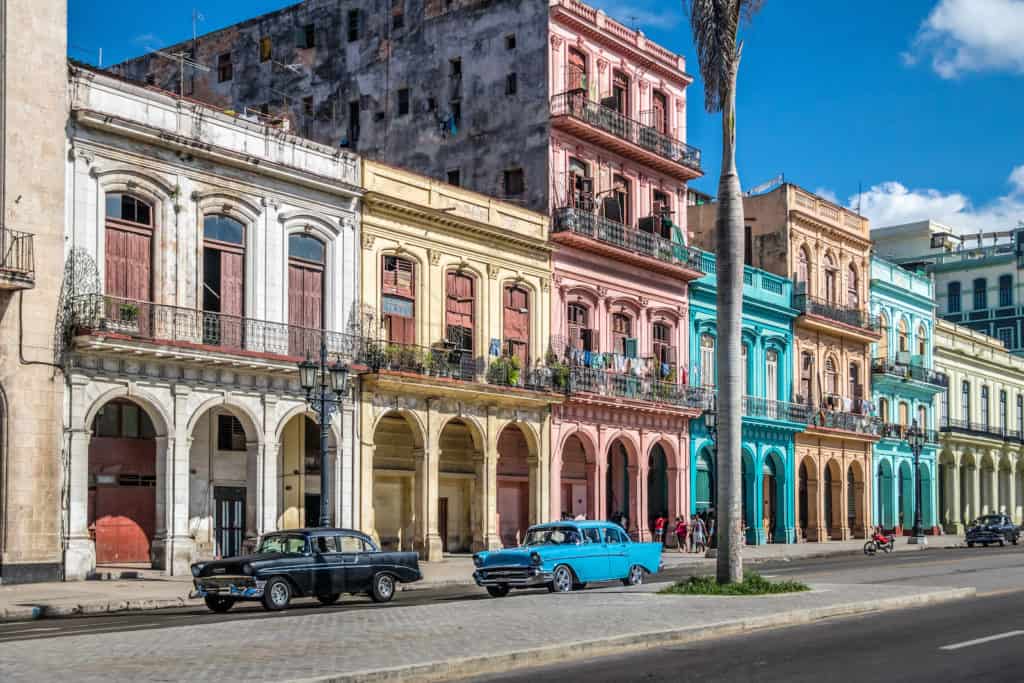 Vintage cars parked in front of colorful historic buildings.