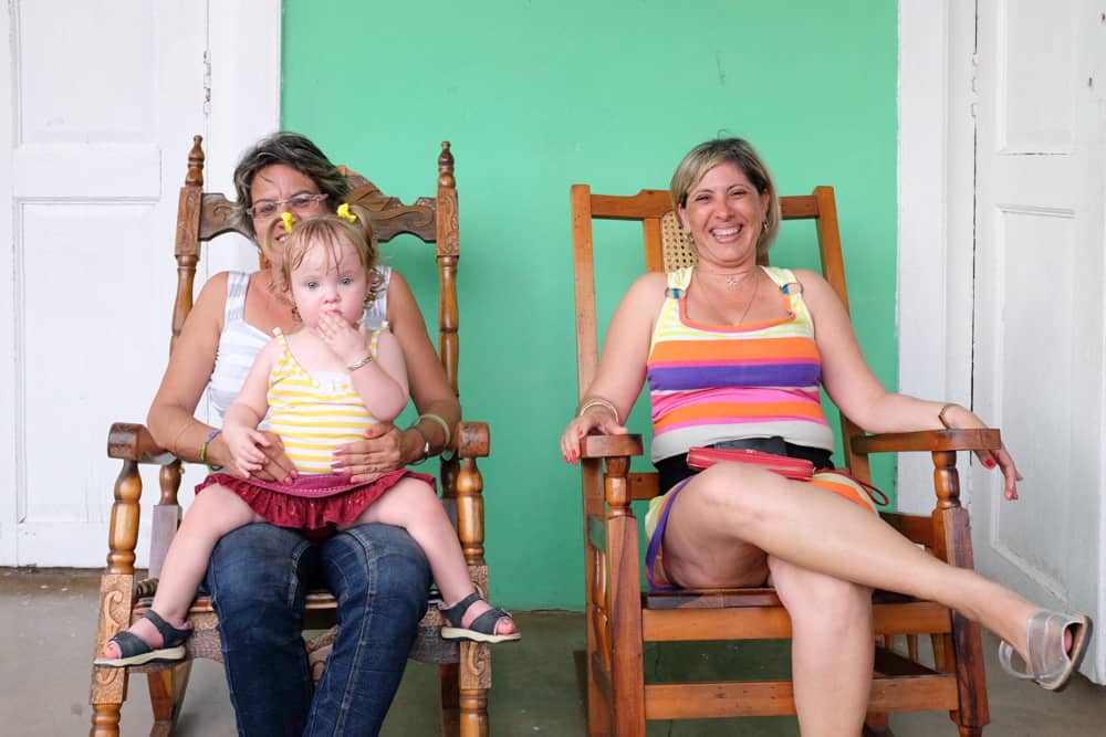 Women and toddler girl sit in rocking chairs.