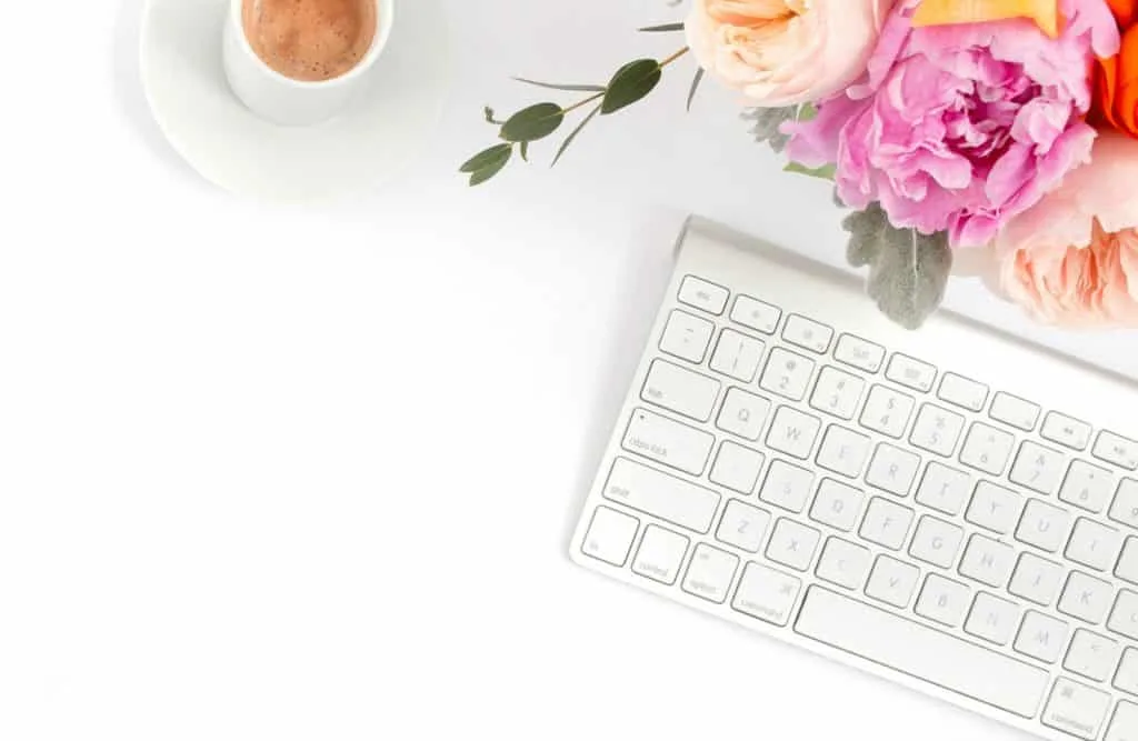 Vase of flowers next to computer keyboard and coffee mug.