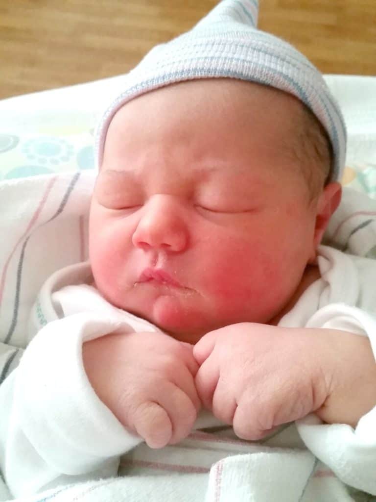 Newborn sleeps in hospital cap.