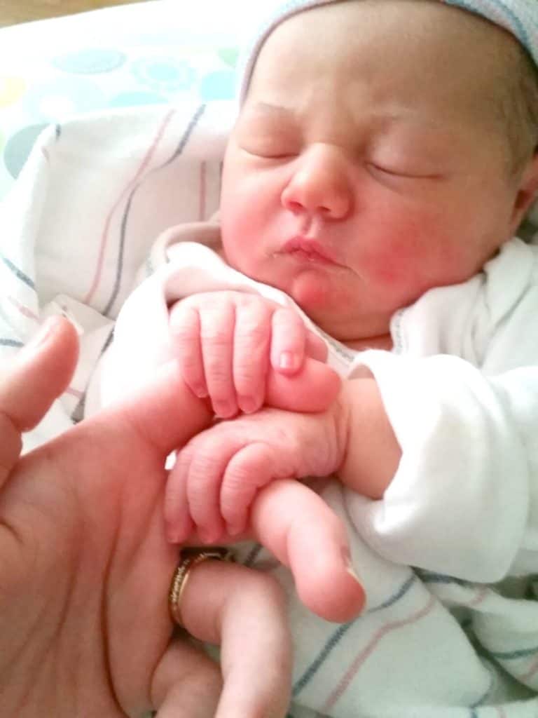Newborn wraps hands around fingers while sleeping.