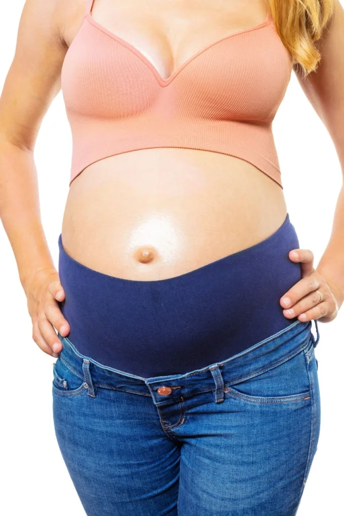 A woman in a pink bra and maternity jeans on a white background.