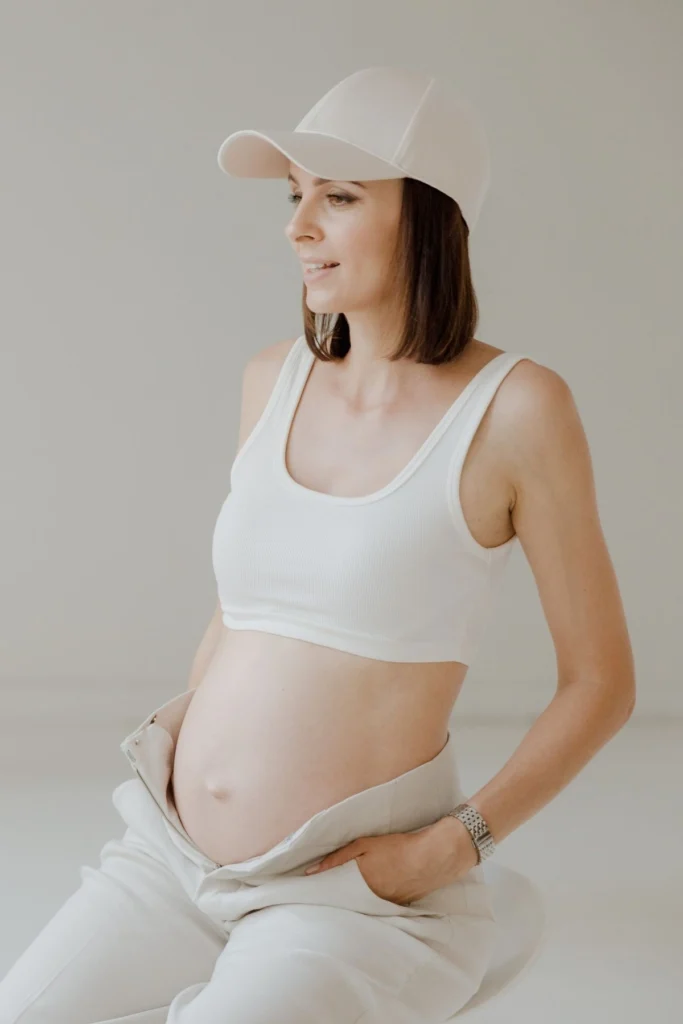 Pregnant woman in a white bra and cream maternity pants.