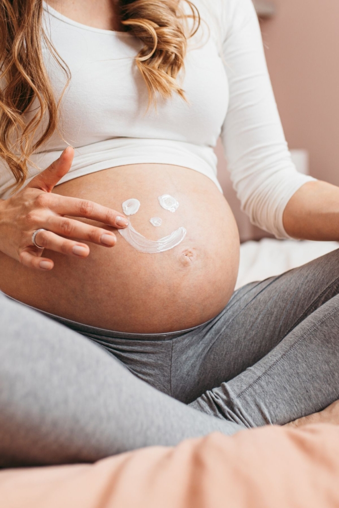 A woman rubs cream in a smiley face on her pregnant belly.