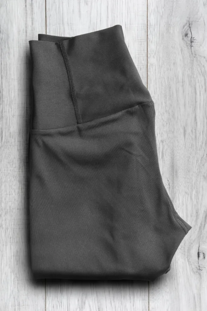 Black folded leggings on a gray wash wood background.