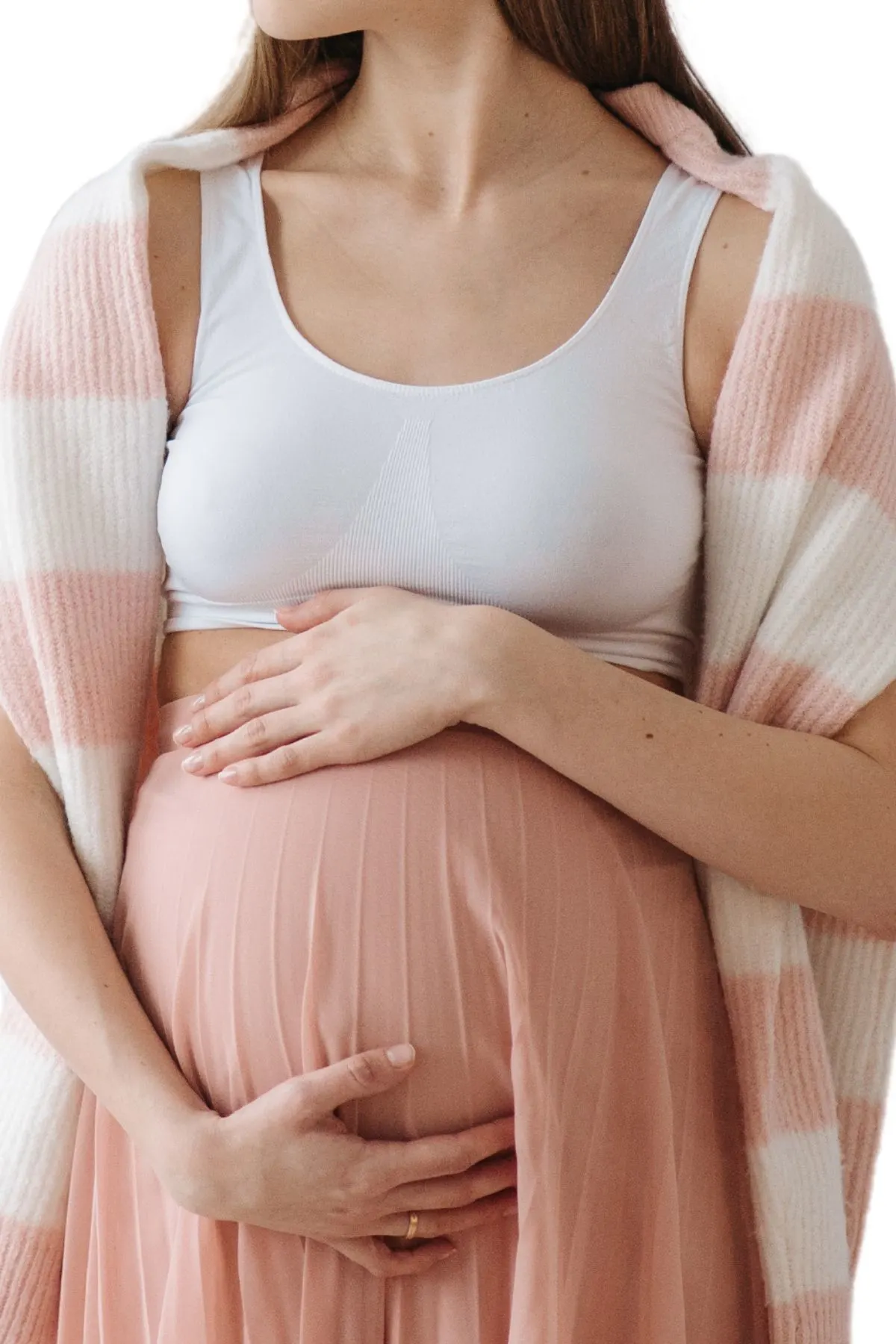 A woman in a white top, pink and white striped cardigan, and pink skirt cradles her pregnant belly.