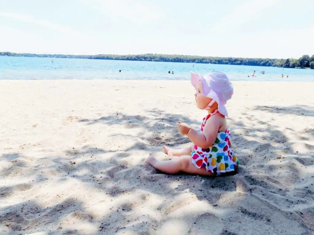 Baby girl sits on beach.