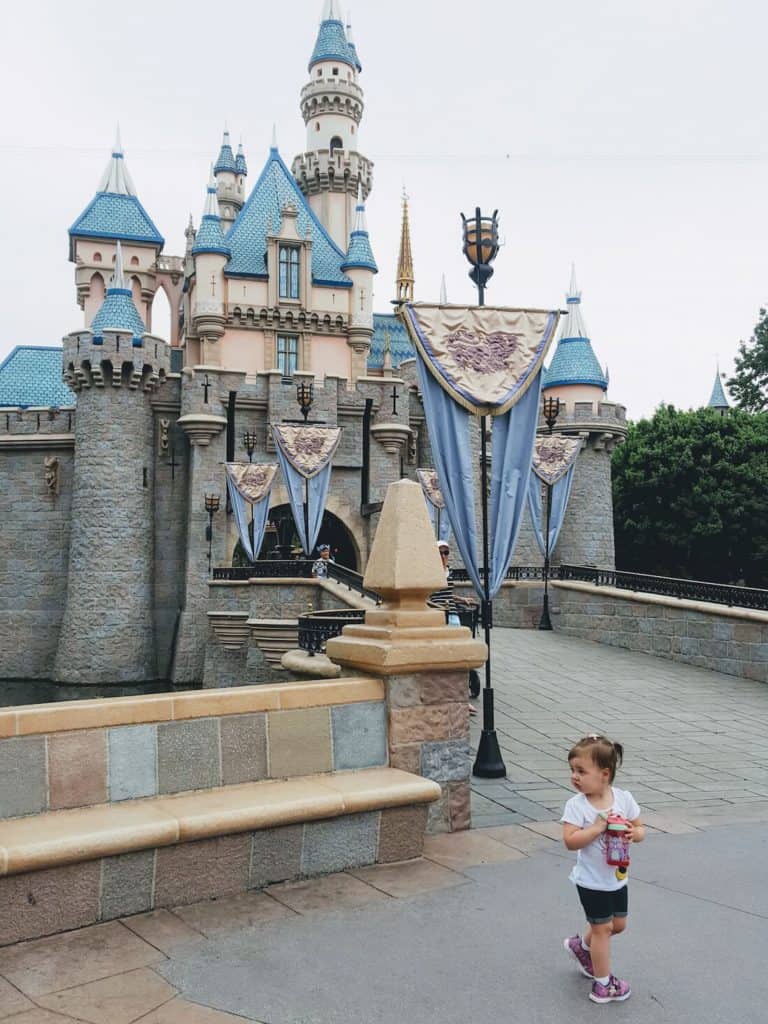 Toddler girl walks in front of Disney Castle.