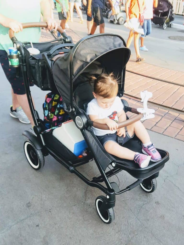 Little girl is pushed in stroller at Disney park.