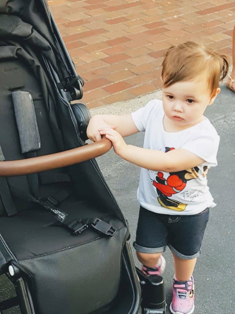 Toddler girl stands next to Austlen stroller at Disney.