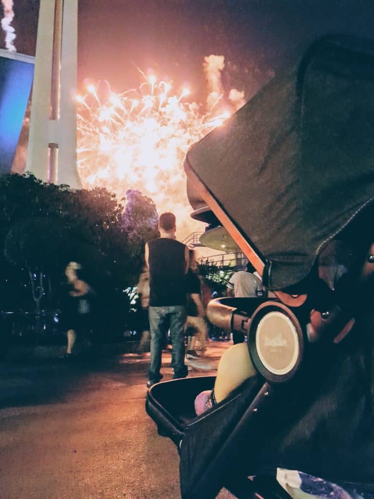 Toddler girl watches fire works from stroller at Disney park.