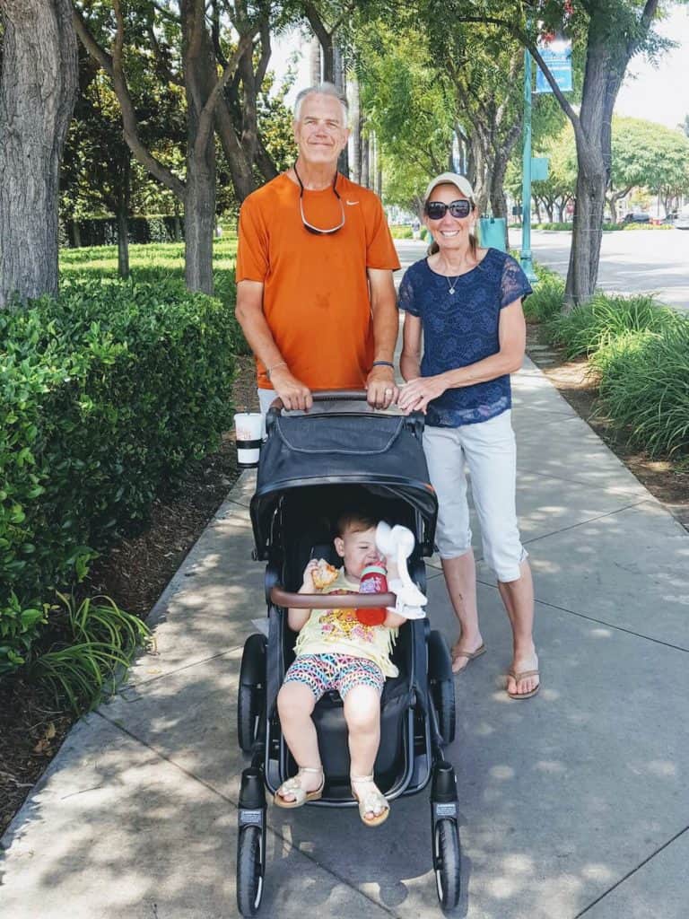 Grandparents push toddler in stroller down paved lane.