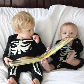 Baby and toddler read book in skeleton Halloween costumes.
