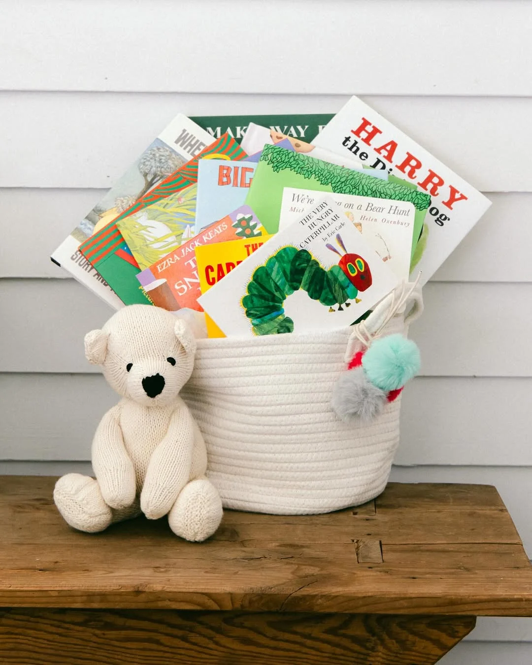 A woven cloth basket filled with children's books on a side table with a stuffed bear.