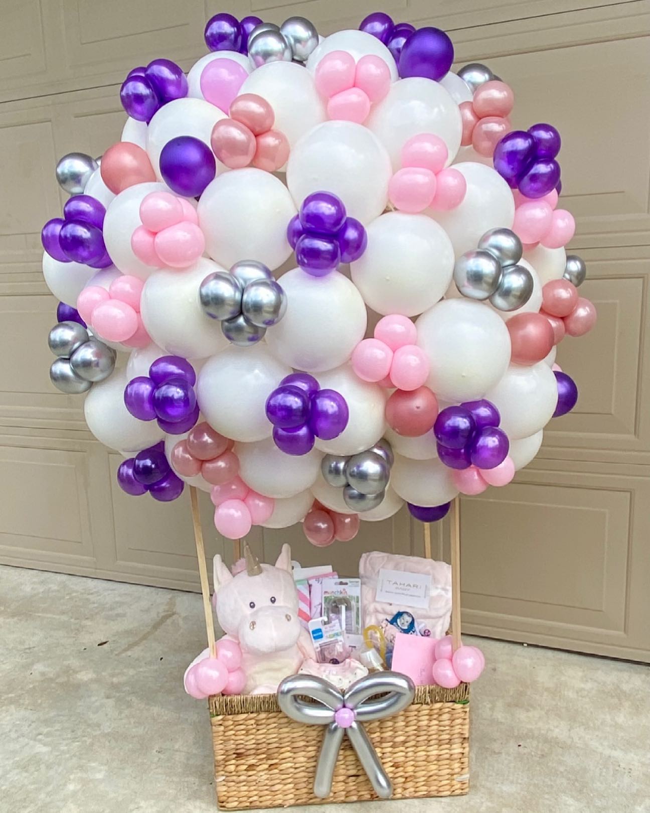 A hot air balloon baby shower gift basket with white, pink, purple, and silver balloons.