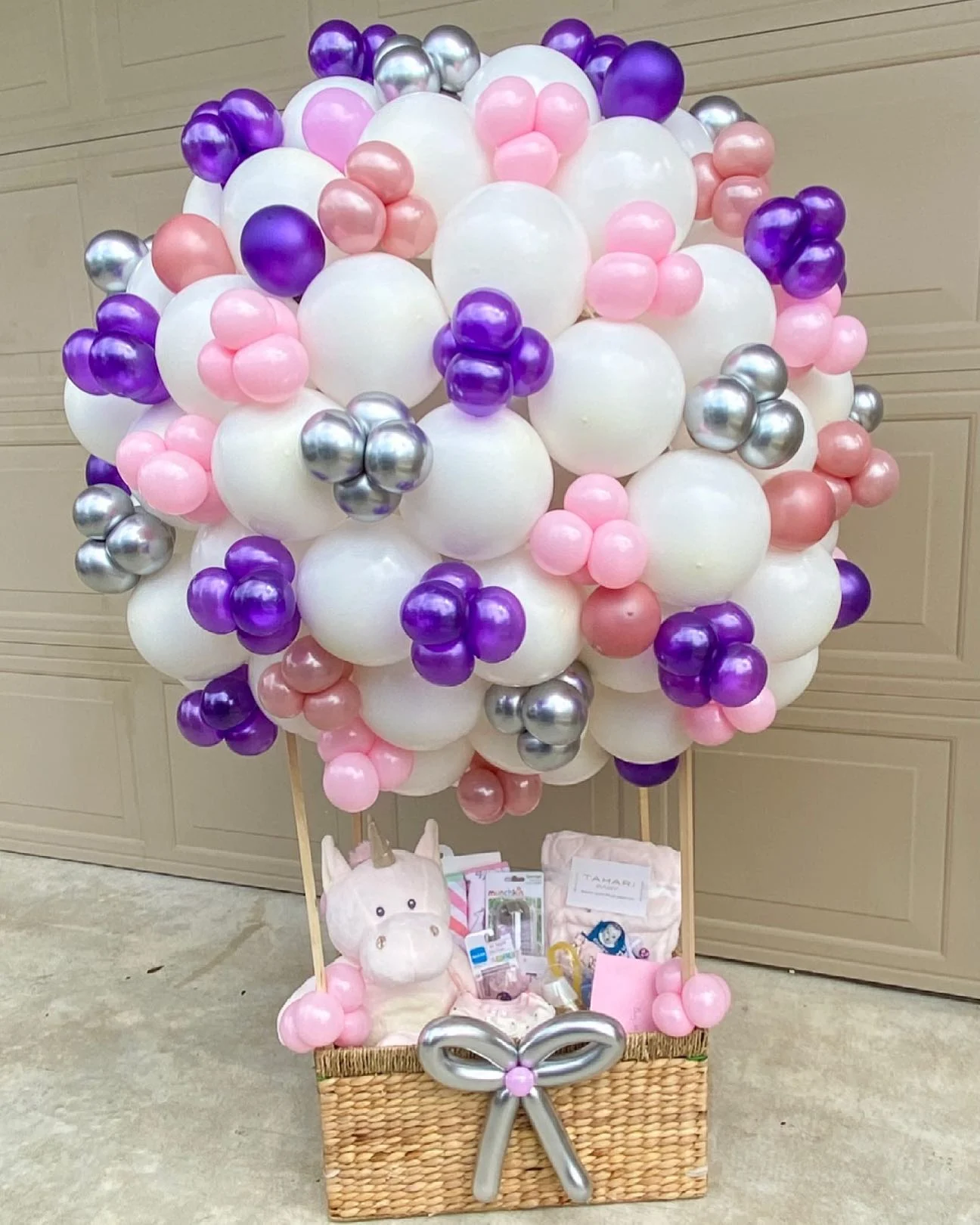 A hot air balloon baby shower gift basket with white, pink, purple, and silver balloons.