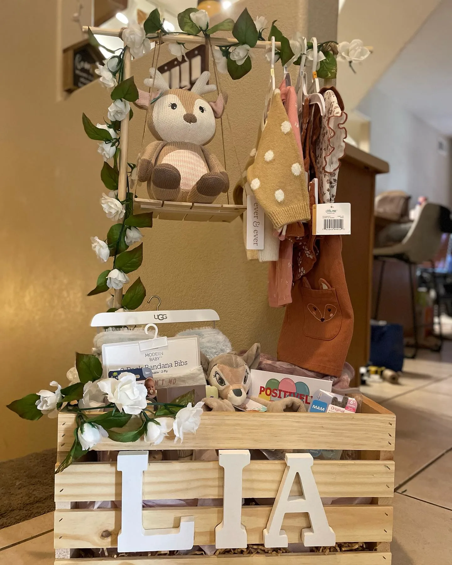 A baby shower gift basket made from a wooden crate with a hanging rod and flowers.