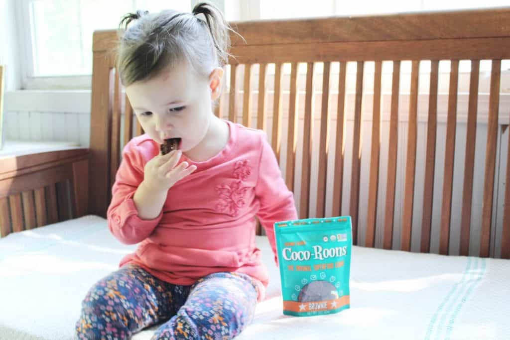 Little girl eats chocolate cookie on indoor bench.