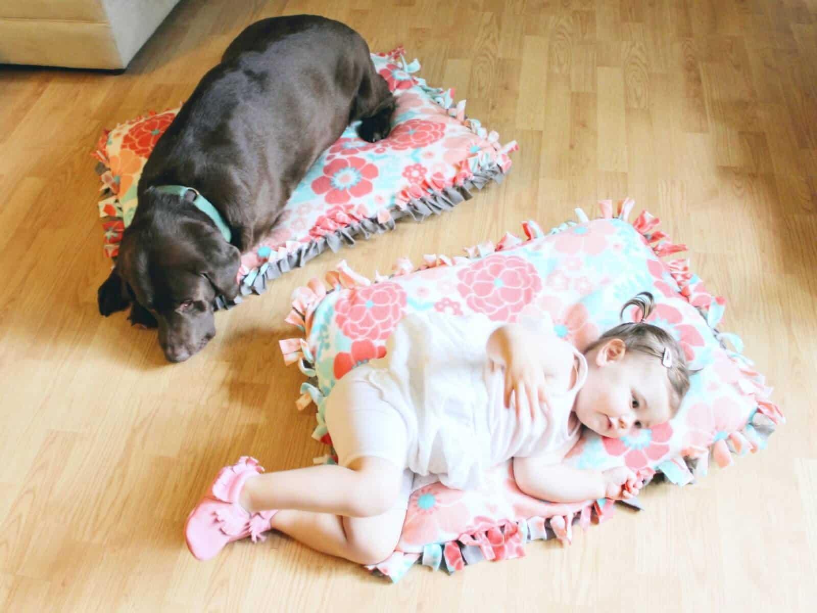 Toddler girl and dog lay on matching floor pillows.