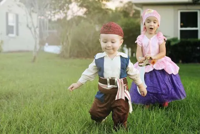 Brother and sister in pirate costumes run through yard.