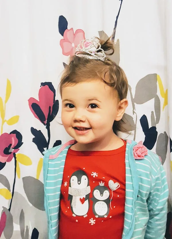 Toddler girl smiles at camera while wearing mini tiara.