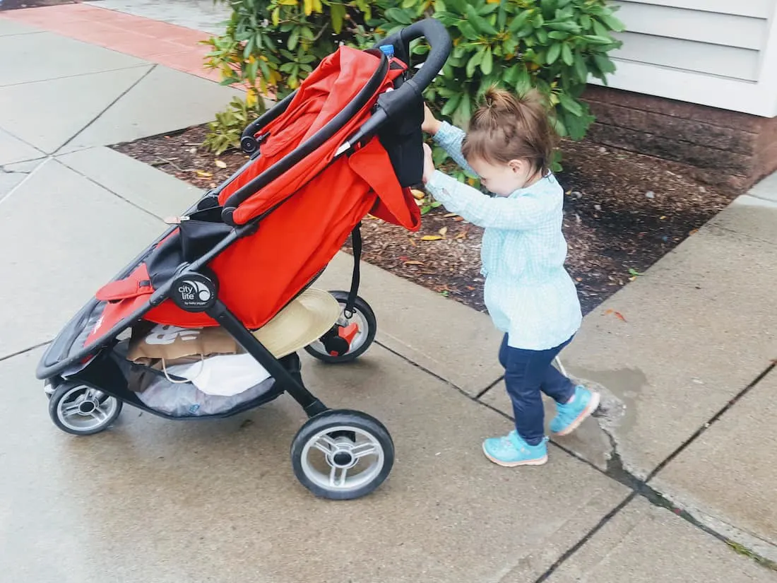 Toddler girl pushes stroller down sidewalk.