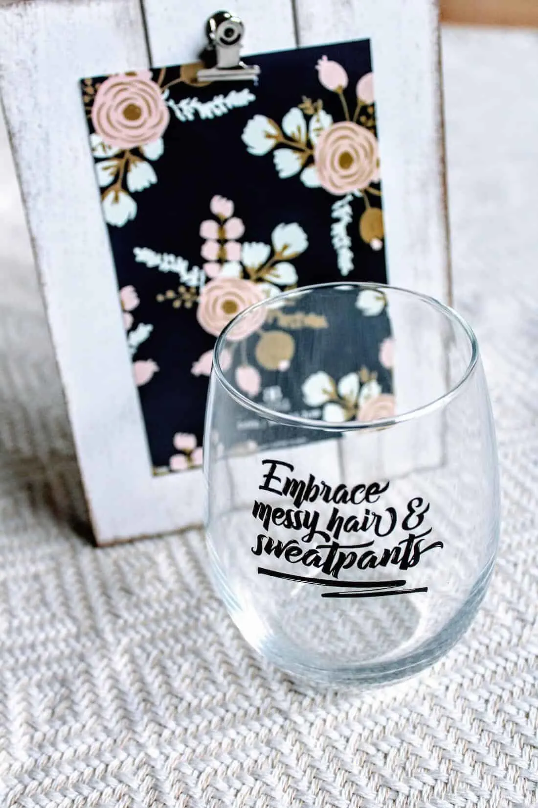 Embrace messy hair and sweatpants wine glass next to picture frame for gift basket.