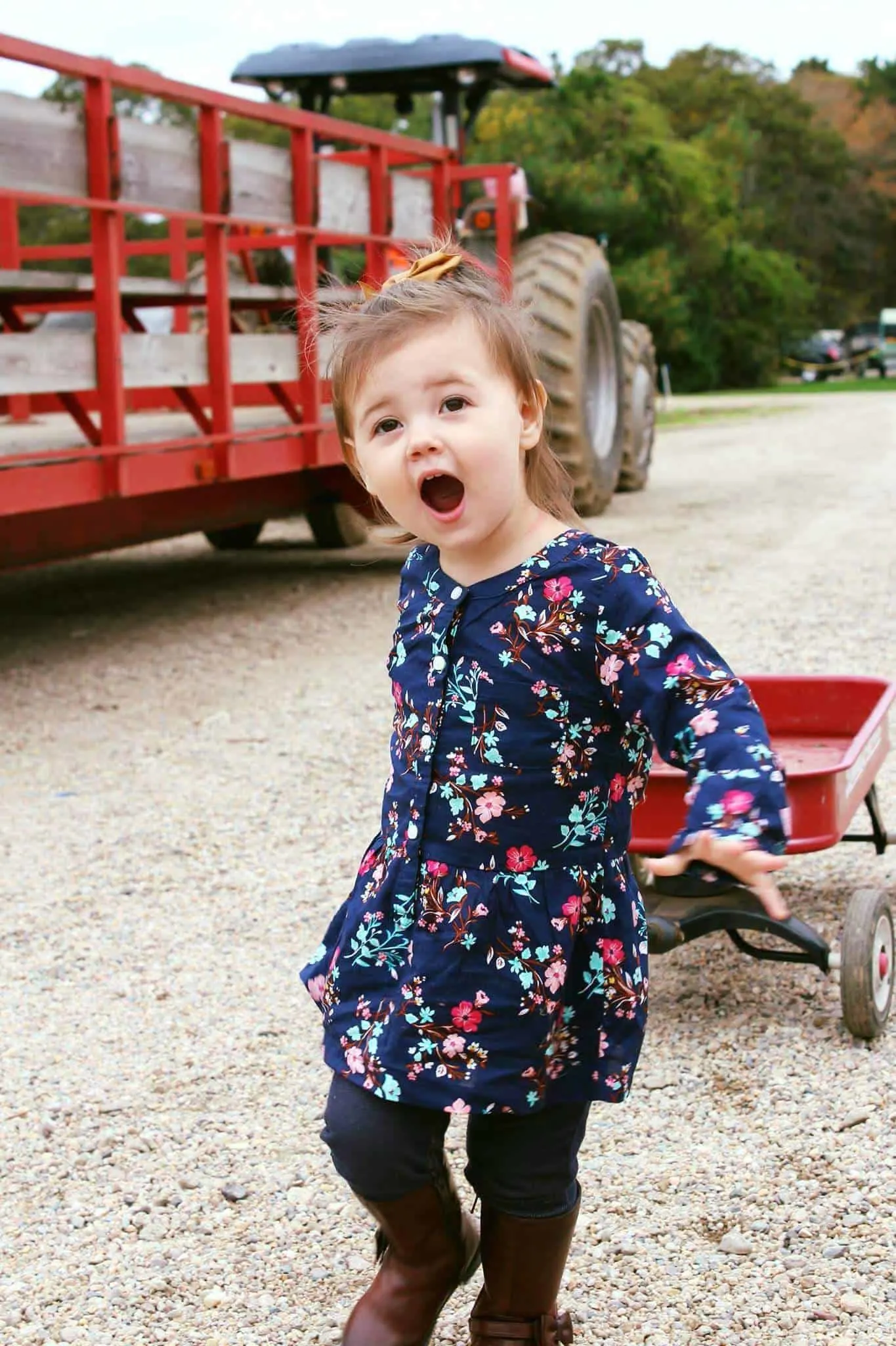 Toddler girl pulls wagon down dirt road.