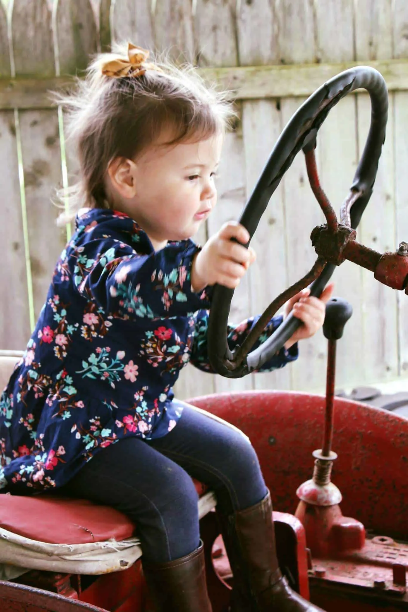 Toddler girl plays with the steering wheel of pumpkin patch tractor.