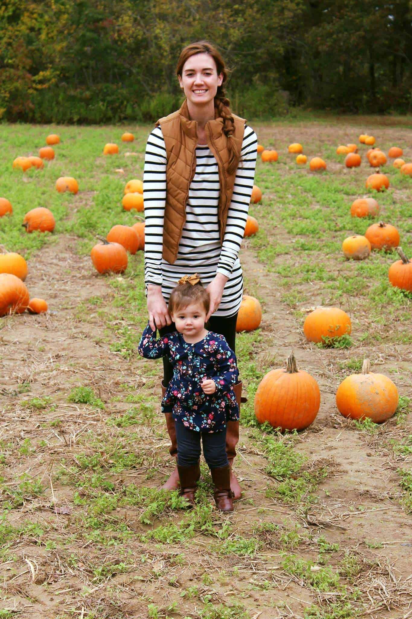 Mom and daughter pose in pumpkin patch.