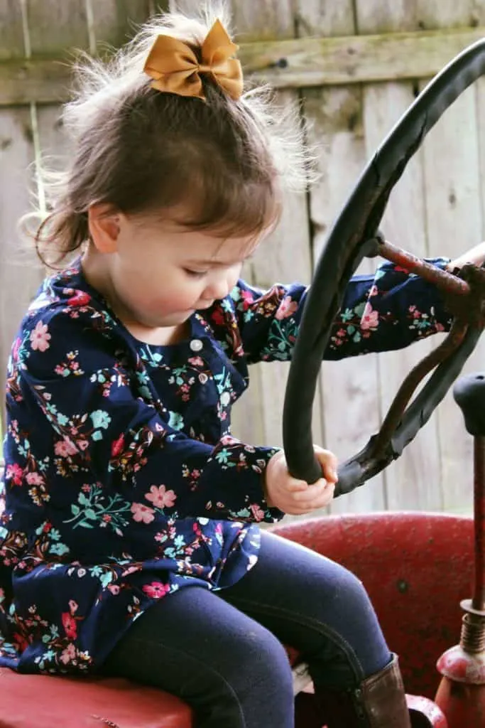 Toddler girl plays on tractor at farm.