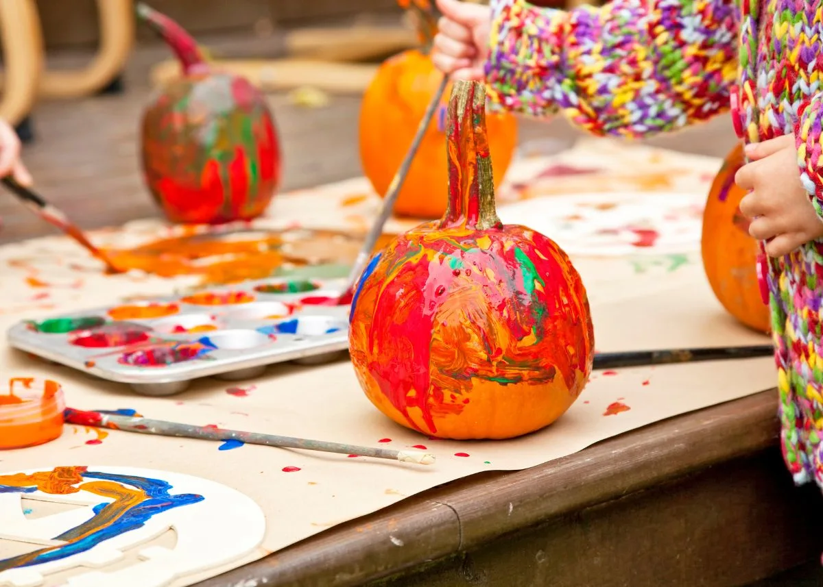 Kids paining pumpkins outside on a table.