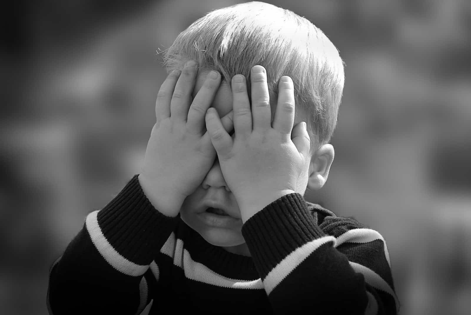 Black and white picture of toddler boy with hands covering his face.