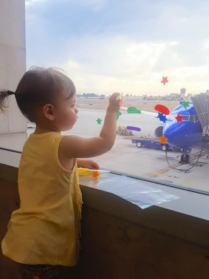 Toddler plays with stickers on airport window.